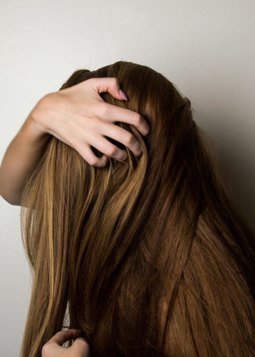 An artistic close-up of a woman's long brunette hair held gently by her hand, emphasizing texture and color.